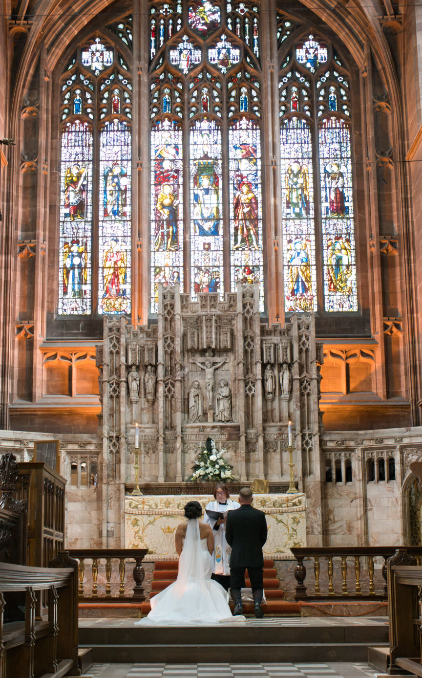 A bride and groom kneeling in front of the beautiful high altar at St George's Church London Road, Stockport