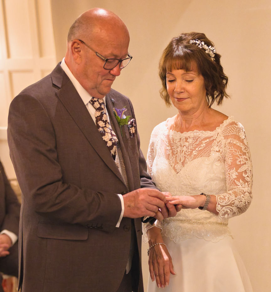A mature groom placing the ring on his bride's finger in the grill room inside Stanneylands Hotel Wilmslow