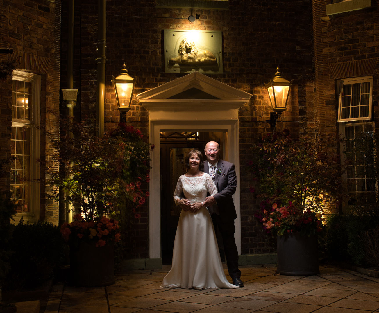 A bride and groom stand out there the entrance of the Stanneylands Hotel Wilmslow at night 